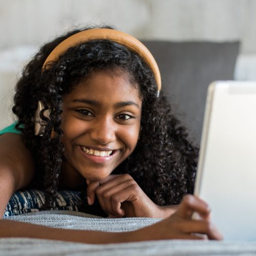 Beautiful happy black teenage girl with headphones on bed reading a book